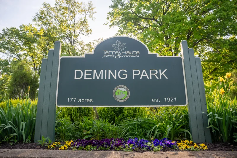 Deming Park entrance sign surrounded by flowers and mature trees