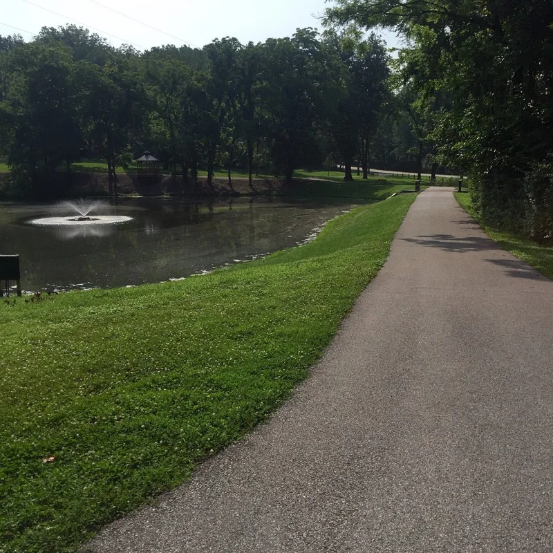 A paved path beside a pond and fountain in Deming Park